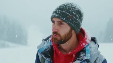 Yeşil örgü şapkalı yakışıklı genç sakallı adamın portresi kar ormanlarında kameraya bakıyor. Çekici bir doğa. Kapatın. Yavaş çekim