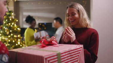 Gülümseyen çok ırklı arkadaşlar kucaklaşarak ailelerine hediyeler getiriyorlar. Kış tatilinin tadını çıkarıyorlar. Mutlu ol. Noel ağacı. Kutlama selamı. Yavaş çekim