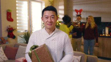 Yakışıklı Asyalı genç adam Noel hediyesine gülümseyen kameraya bakar süslü Noel odasındaki kameraya. Kış tatilinin tadını çıkarıyorum. Yeni yıl. Kutlama yapalım. Yavaş çekim
