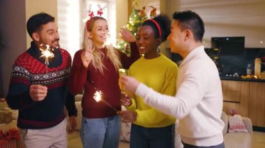 Bir grup çok ırklı arkadaş, ellerinde yanan maytaplarla Noel 'de dans ederken kameraya bakıyorlar. Geleneksel tatil. Kutlama. Mutlu noeller. Kış zamanı. Yavaş çekim