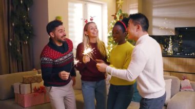 Yanan maytaplarla Noel 'de rol alan çok ırklı genç arkadaşların portresi evdeki kameraya bakıyor. Geleneksel tatil. Kutlama. Mutlu noeller. Kış zamanı. Yavaş çekim