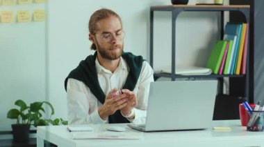 Gözlüklü çekici genç adam dizüstü bilgisayarlı iş yeri karantinası bilgisayar hijyenik ofis çalışanı ağır çekimde çalışmadan önce antiseptikle elleri dezenfekte ediyor.