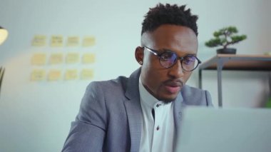 Gülümseyen Afro-Amerikan yakışıklı adam modern ofis programcılarında bilgisayar kullanıyor. Monitörde başarılı çalışan işadamına bakıyor. Mühendislik problemlerini yavaş çekimde çözüyor.