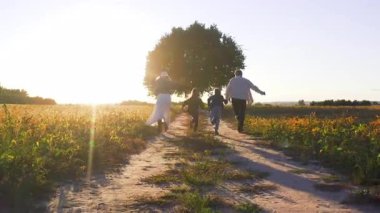 Aile resimli doğada vakit geçirir. Güzel çocukları olan neşeli bir ebeveyn büyük ağaca doğru hızla koşarken eğleniyor..