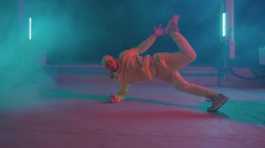 Yakışıklı break dansçı hip hop sanatçısı dumanlı çatıda breakdance tarzı dans yapıyor. Neon gece performansı.