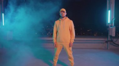 Gece dumanında poz veren parlak sarı kıyafetli yakışıklı hip hop dansçısının tam boy portresi. Sahne performansı. Sanatçı. İnsanlar.