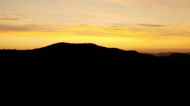 Gün batımında uçan kuş bakışı dağlar. Resmedilmeye değer koyu siyah dağlar, kırmızı renkli gökyüzü altında ormanlar. İHA uçuşu. Seyahat.