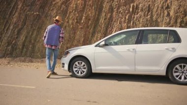 Araba arızası. Hüsrana uğramış sakallı adam arabasını durduruyor, dışarı çıkıyor ve motor hasarını inceliyor. Yolda bir kaza oldu. Kırsal.