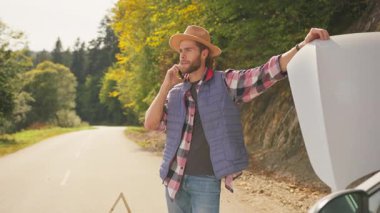 Kafkasyalı stresli, endişeli bir genç adam telefonda bozuk bir arabanın yanında konuşuyor. Şehir yolunda araba arızası..