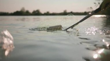 Gezegeni kurtar. Birisinin çöp toplamak için balık ağını kullandığı sahne. Su kirliliği. Çevre. Doğa. Yakın çekim..