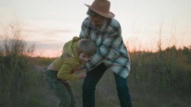Neşeli, komik, beyaz sakallı baba ve küçük oğlu açık havada yakalama oyunu oynuyorlar. Aile buğday tarlasında. Köy doğası. Yaz zamanı..