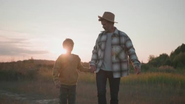Güzel bir gün batımında açık buğday tarlasında yürüyen sevimli oğlu olan mutlu beyaz bir baba. Güzel bir aile portresi. Maceralar. Yaz zamanı. Köy.