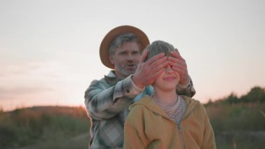 Sakallı mutlu baba orta yaşlı adam, sevimli güneşini korkutmak için gözlerini kapatıyor ve birlikte eğleniyorlar. Yürüyorum. Köy. Aile ilişkisi. Portreler.