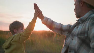 Köydeki aile. Sevecen bir baba oğluyla birlikte sahada yürüyor, beşlik çakıyor ve açık doğada yaz akşamı macerasının tadını çıkarıyor. Takım. İlişki.