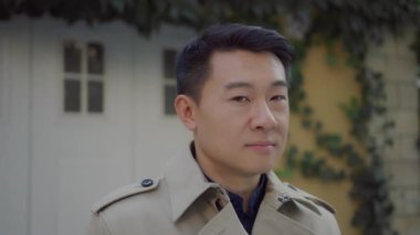 Zengin, yakışıklı, başarılı, genç bir iş adamı. Güz ceket giyiyor. Evin yanında duruyor ve gülümsüyor..