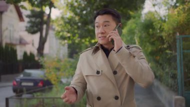 Palto giymiş Asyalı yakışıklı zengin işadamı güz sokağında iş arkadaşıyla cep telefonu paylaşımı hakkında konuşuyor. Kariyer insanları. Başarı. Teknoloji.
