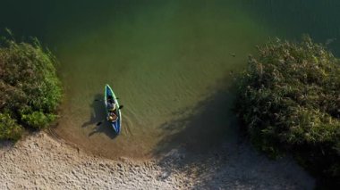 Genç bir ailenin insansız hava aracı huzurlu gölde birlikte kayak yapıyor. Baba ve oğul, şişme kayıkla nehrin karşısına geçmek için antrenman yapıyorlar. Üst uçuş görünümü.