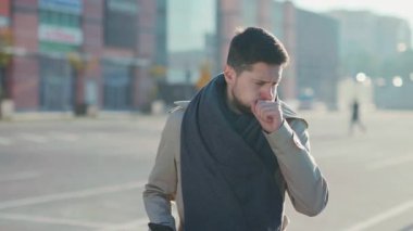 Hasta alerjik, sağlıksız, beyaz sakallı, yakışıklı bir adam öksürüyor, hapşırıyor ve dışarıda telefon kullanıyor. Sonbahar havası. Hastalık. Salgın. Coronavirüs.