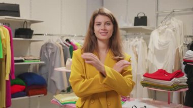 İç mekan portresi. Moda tarzı giyinmiş çekici bir kadın. Bir giyim mağazasında kollarını kavuşturarak gülümsüyor..