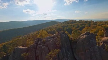 Resimli doğada FPV uçuşu ilham verici. Sonbahar ormanının hava manzarası, güzel mavi gökyüzü ve kayalık tepeler. Uçurumun tepesindeki genç adam kollarını kaldırarak özgürlük yolculuğunun tadını çıkarıyor..