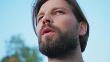 Kapalı hava arka planında sakallı ve bıyıklı yakışıklı beyaz bir adam. Doğaya hayran olan atletik erkek eğitimi. Portreler. Düşünceli. İnsanlar.