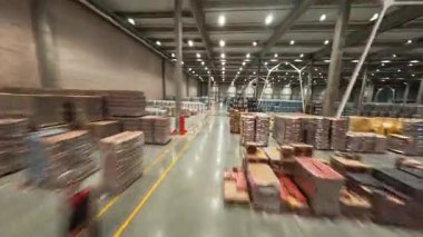 FPV görüntülü İHA lojistik park istasyonunda. Büyük bir sanayi deposu ve sıra sıra mal teslimatı. Kutular ve paketler. Çalışan personel.