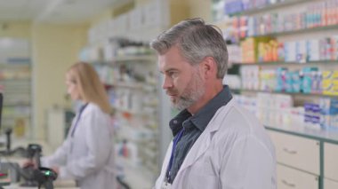 Modern eczacı dükkanında beyaz sakallı, profesyonel, olgun, yetişkin bir erkek eczacıya yakın çekim. Eczanede danışman. Eczacı..