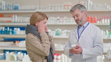 Eczanedeki hasta sarışın kadın, baş ağrısı ve virüs belirtilerinden şikayetçi, eczacıdan ilaç alıyor. Tıbbi reçete. Eczane. Danışma.