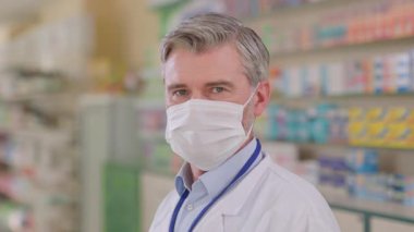 Kafkasyalı gri saçlı yetişkin doktor eczane danışmanı tıbbi koruyucu maske takıyor. Koronavirüs salgını. Sağlık görevlileri. Eczane.