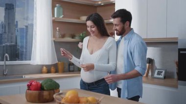 Mutfaktaki ultrasonografi çocuk röntgen fotoğrafına bakan beyaz, genç bir aile babası ve hamile bir eş. Konforlu evde mutlu ve hevesli bir çift..