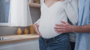 Genç, evli, müstakbel ebeveynler mutfaklarında birbirlerine sarılıyorlar. Mutlu koca hamile karısını kucaklıyor. Güven ilişkisi. Planlanmış hamilelik.