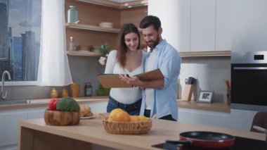 Mutlu bir çift hamile kadın ve sakallı bir adam modern mutfakta aile albümünün fotoğraflarını inceliyor. İç mekan. Aile hayatı. İlişki.