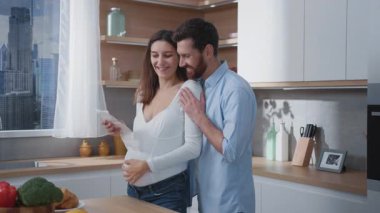 Gelecekteki sevecen anne babaların neşeli beyaz çifti hamile eş ve kocalar modern şık ev mutfağında ultrason fotoğraflarını izliyorlar..