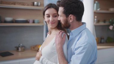 Sevecen bir çift, mutfakta bebek bekleyen ve sıkı sıkı sarılıp konuşan karısına ve kocasına hamile. Aile anları. Planlanmış hamilelik.