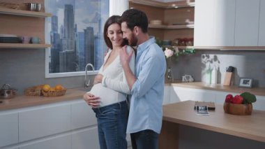 Genç, sevecen, sakallı, beyaz, hamile ve çekici karısı mutfakta kucaklaşan bir çift. Harika bir aile sahnesi. Rahat bir ev. İlişkiler.
