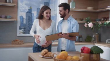Güzel, genç, hamile bir eş ve kocası şık mutfaklarında aile albümlerini inceliyor. Modern yaşam tarzı. Aile hayatı. İlişki.