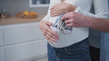 Aile hayatı. Genç bir çift hamile eşi kucaklıyor nazikçe sarılıyorlar ve küçük şirin bebek ayakkabıları tutuyorlar. Portreler. Planlı hamilelik. Nesiller.