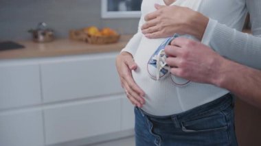 Beyaz, genç, neşeli bir aile çifti hamile bir eş kocasına sarılıyor ve küçük bebek ayakkabıları tutuyor. Hayat amacı partnerleri. Planlanmış hamilelik.