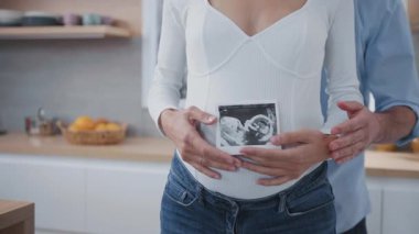Yakın plan hamile, çekici bir kadın elinde ultrason fotoğrafıyla kocasına sarılmış bir bebeği olduğu için mutlu. Aile ilişkisi. Ebeveynlik.