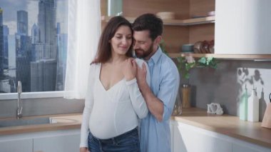 Sevgi dolu genç bir çiftin sevimli aile sahnesi. Gelecekteki ebeveynler kucaklaşıp rahat bir mutfakta kalıyorlar. Ev hayatı. Aile ilişkisi. Hamilelik. Ebeveynlik.
