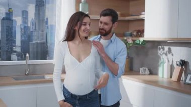 Aile hayatı. Neşeli bir çift Kafkasyalı genç ebeveyn, mutfakta çocuk kucaklaşması bekliyor. Hamile bir kadın. Sağlık hizmetleri. Ebeveynlik kavramı.