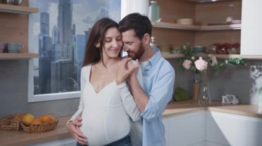 Beyaz tenli, mutlu, gülümseyen, sakallı, genç baba koca ve güzel hamile karısı mutfakta. İlişki hedefleri. Sağlıklı planlanmış hamilelik.