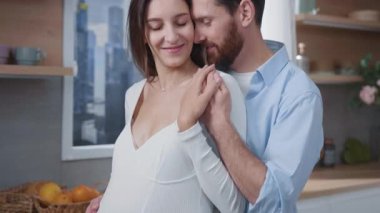 Yakışıklı, mutlu, müstakbel ebeveynler, bir çocuğun el ele tutuşmasını bekliyorlar. Evde bebeğin karnına nazikçe dokunuyorlar. İç mekanlar. Mutfağa. İlişki. Aileler.