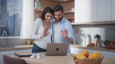 Kafkasyalı bir çift neşeli karı koca hamilelik haberlerini arkadaşlarıyla görüntülü sohbet ederek paylaşmayı bekliyor. Laptop mutfakta. Aile hayatı. Ebeveynlik.