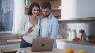 Genç, çekici ve mutlu bir aile dizüstü bilgisayarda bebek sohbeti bekliyor. Evli ve neşeli çift hamilelik haberlerini aileleriyle paylaşıyor..