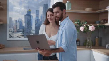 Mutlu ebeveynler dizüstü bilgisayarlarını kullanarak gelecekteki bebekleri için alışveriş kıyafetlerini arıyorlar. Hamilelik. Aileler. İletişim.