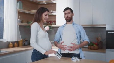 Aile hayatı. Hamile, mutlu bir kadın kocasının hamile taklidi yapmasına gülüyor. Genç ebeveynler. Ev mutfağı..