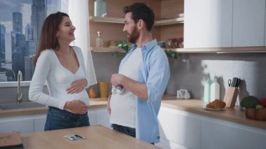 Neşeli bir çift, mutfaktaki sıcaklıkta birlikte heyecanlı hamilelik yolculuklarını kucaklıyor.