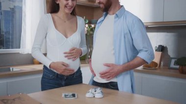 Neşeli bir çift güzel tasarlanmış bir mutfakta harika bebek ayakkabılarıyla heyecanlı hamileliklerini kutluyor.