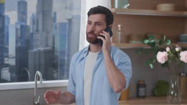 Genç bir adam, modern bir mutfak içinde şehir manzarası sunan bir telefon görüşmesi yapıyor.
